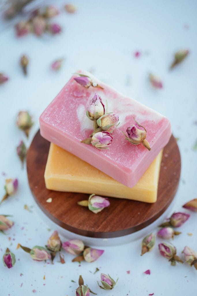 7 Bath Essentials to keep in your Bath Time Close-up of two handmade soaps adorned with rosebuds, resting on wooden dish.