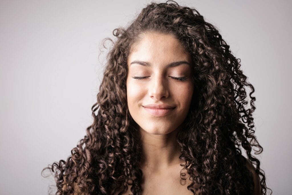 A close-up portrait of a smiling woman with curly hair, eyes closed, exuding happiness.