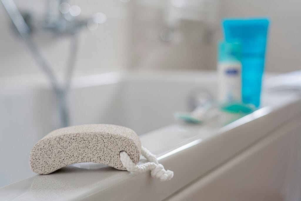 7 Bath Essentials to keep in your Bath Time A pumice stone placed on a bathtub edge, ideal for foot care in a contemporary bathroom setting.