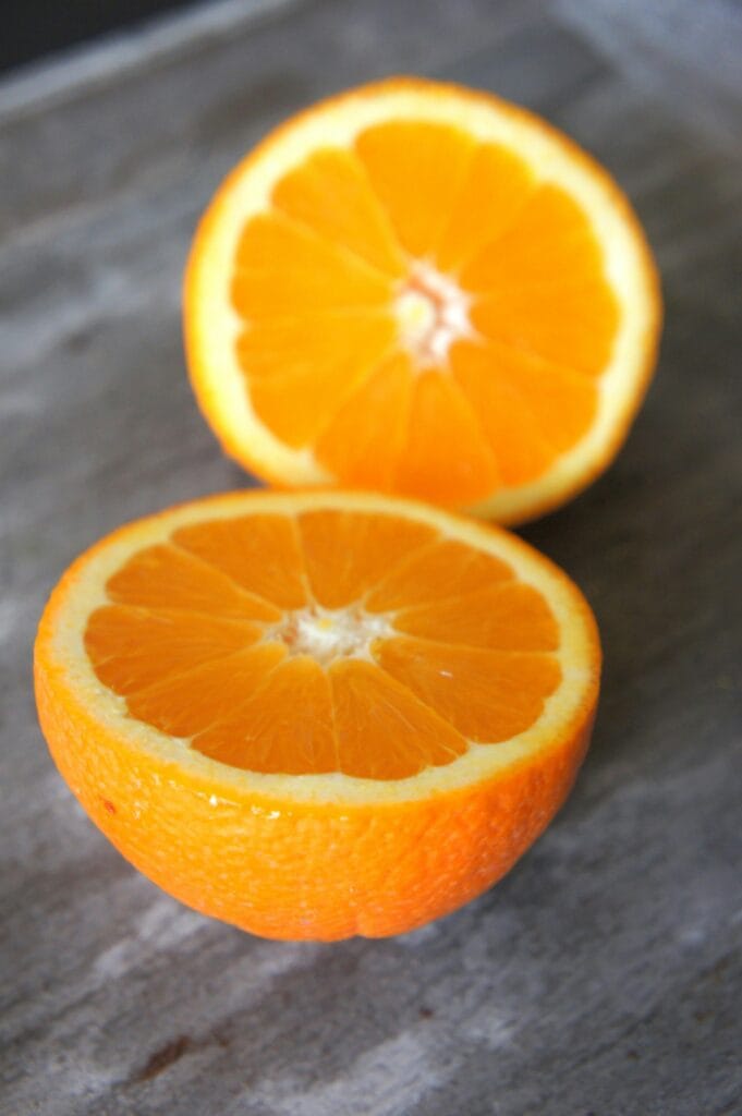10 Essential Oils for Natural Cleaning Vibrant close-up of two fresh orange slices on a rustic surface, highlighting their juicy texture.