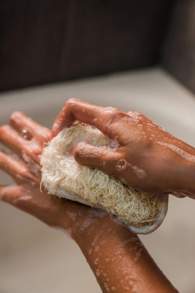 7 Bath Essentials to keep in your Bath Time Hands scrubbing with a loofah in a bath setting, focusing on personal hygiene.